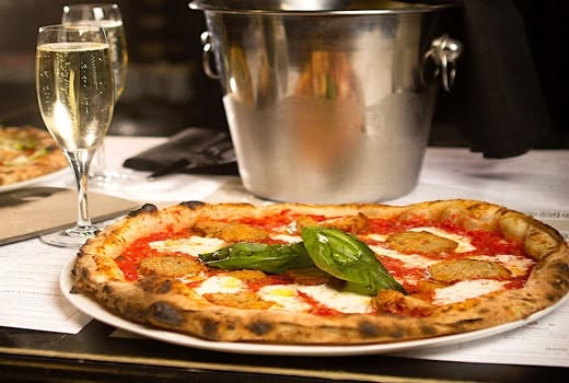 A freshly baked pizza served with a glass of prosecco