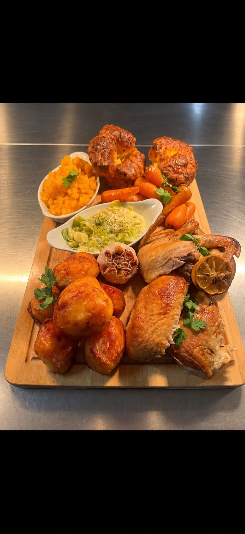 A Sunday roast sharing board with chicken, roast potatoes, Yorkshire puddings and vegetables